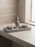 Fotografía editorial minimalista de Buda zen de cemento con velas de loto encendidas en entorno natural con luz suave.